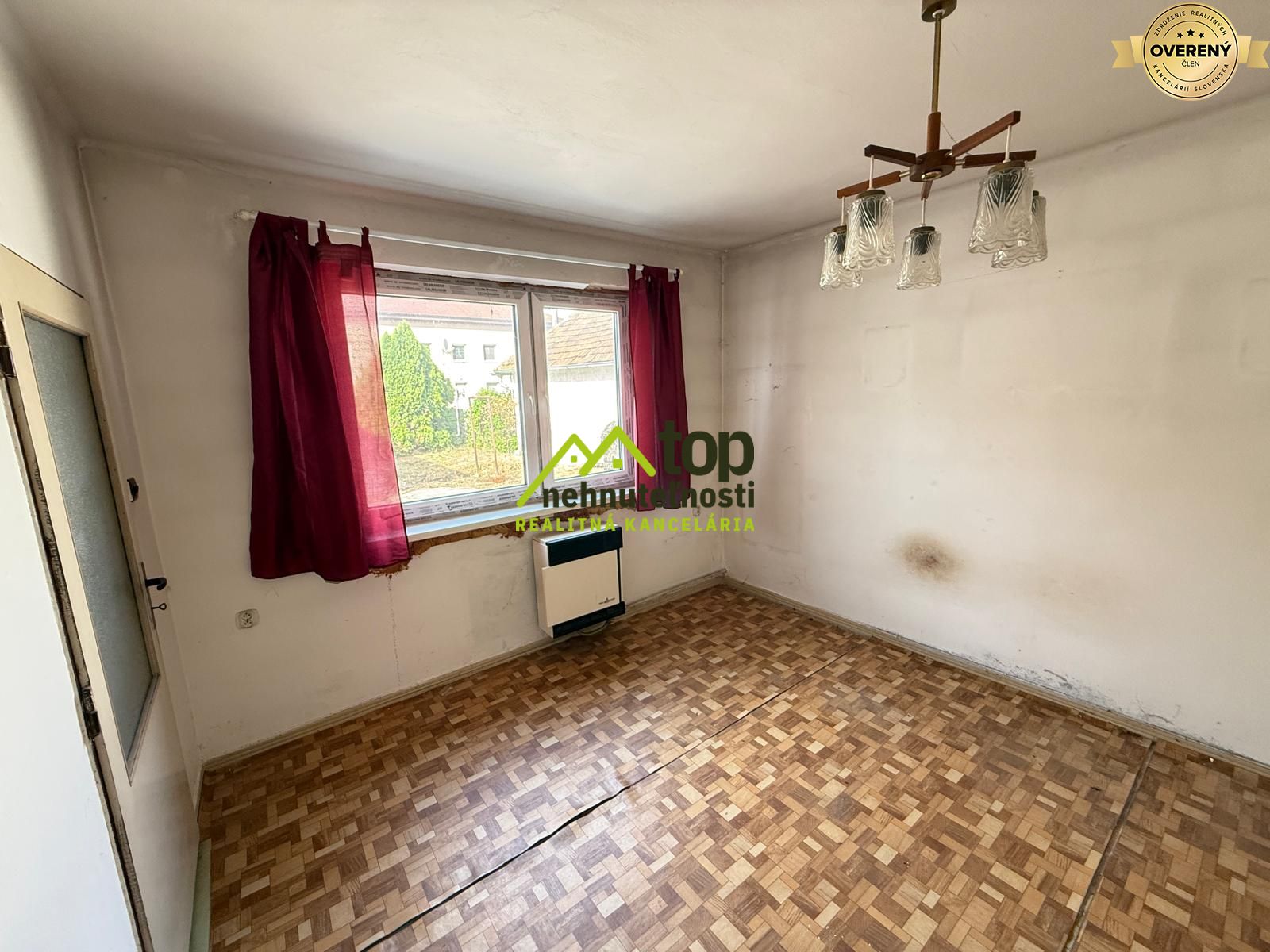 Izba v rodinnom dome s parketovou podlahou, bielymi stenami a červenými závesmi.