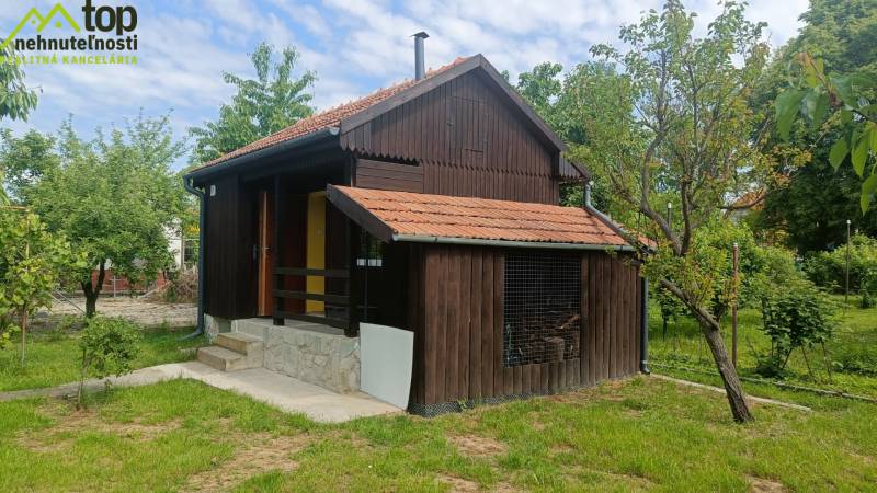 Drevená chatka v záhradách Tovarník obklopená stromami a zeleňou.
