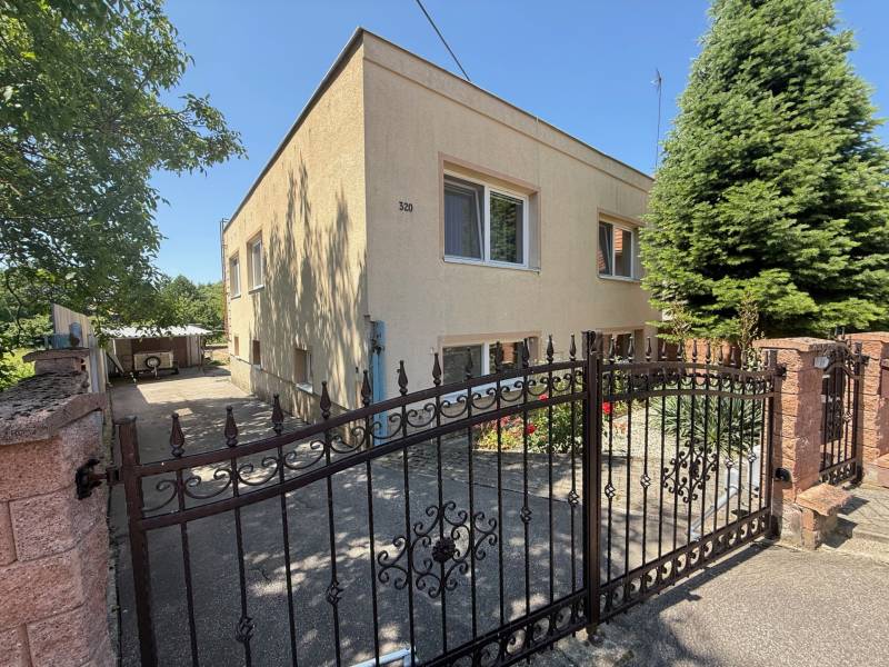 Brána a fasáda rodinného domu v Nemčiciach s ihličnanmi a záhradkou.