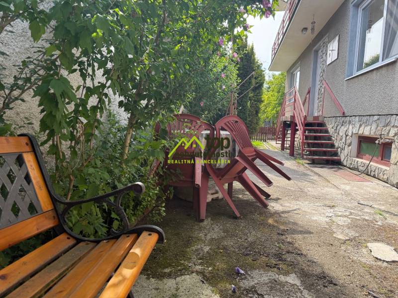 Dvory rodinného domu v Skačanoch s lavičkou a poskladanými stoličkami v záhrade.
